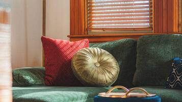 Une pièce avec un canapé vert, un coussin rouge, un pouf doré et bleu, et une lampe sur pied.