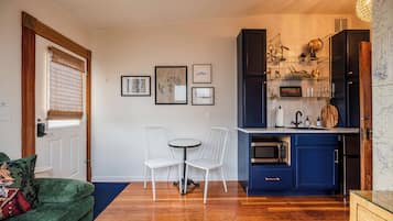 Un espacio habitable compacto con zona de comedor, kitchenette y un rincón de estar acogedor con un sofá verde y alfombra estampada.