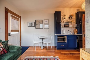 A compact living space with a dining area, a kitchenette, and a cozy seating area with a green sofa and a patterned rug. - The Matriarch| Suite 3 | Pet friendly (Ashland)