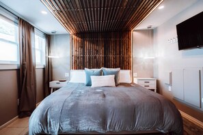 A modern bedroom with a large bed, wooden slatted ceiling, and a flat-screen TV on the wall. - Swank House -Downtown Suite- Pet Friendly (Ashland)