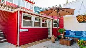 A red building with a sign reading "Downtown Suite," a patio with a blue sofa and wicker furniture, and a hanging planter.