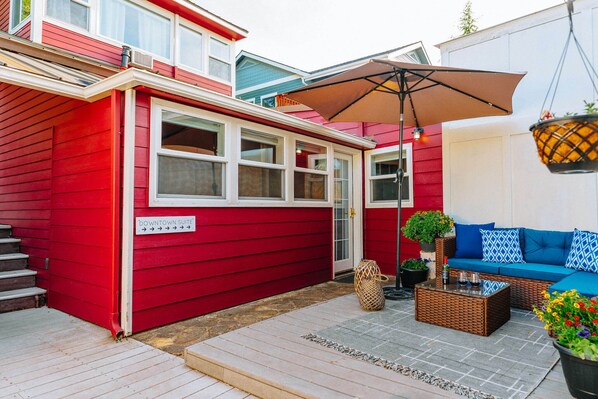 A red building with a sign reading "Downtown Suite," a patio with a blue sofa and wicker furniture, and a hanging planter. - Swank House -Downtown Suite- Pet Friendly (Ashland)