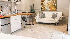 A modern kitchen with a microwave, sink, and dining area. There is a white sofa and a painting on the wall.