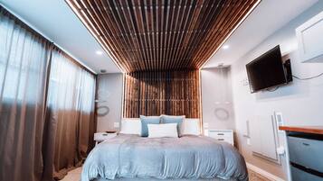 A modern bedroom with a large bed, wooden slatted ceiling, a flat-screen TV, and a built-in wardrobe.