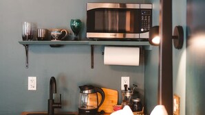 Een keuken met een roestvrijstalen magnetron, een koffiezetapparaat, een waterkoker, en een plank met bekers en een glas.
