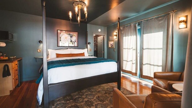 Een slaapkamer met een groot bed, een kroonluchter, een bureau, een stoel en een raam met gordijnen.