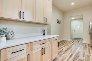 Una cocina con armarios de madera, encimera blanca y suelo de madera.
