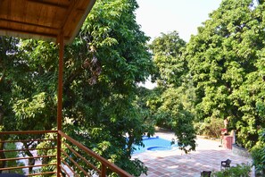 Un espace piscine doté d’une terrasse carrelée, entouré d’arbres verdoyants.