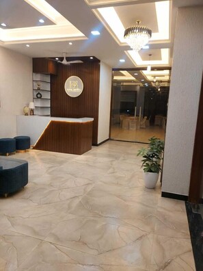 A hotel reception area with a modern design, featuring a reception desk, seating area, and a chandelier.
