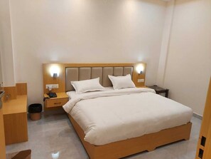 A modern hotel room with a large bed, bedside tables, a wooden nightstand, and a small desk.