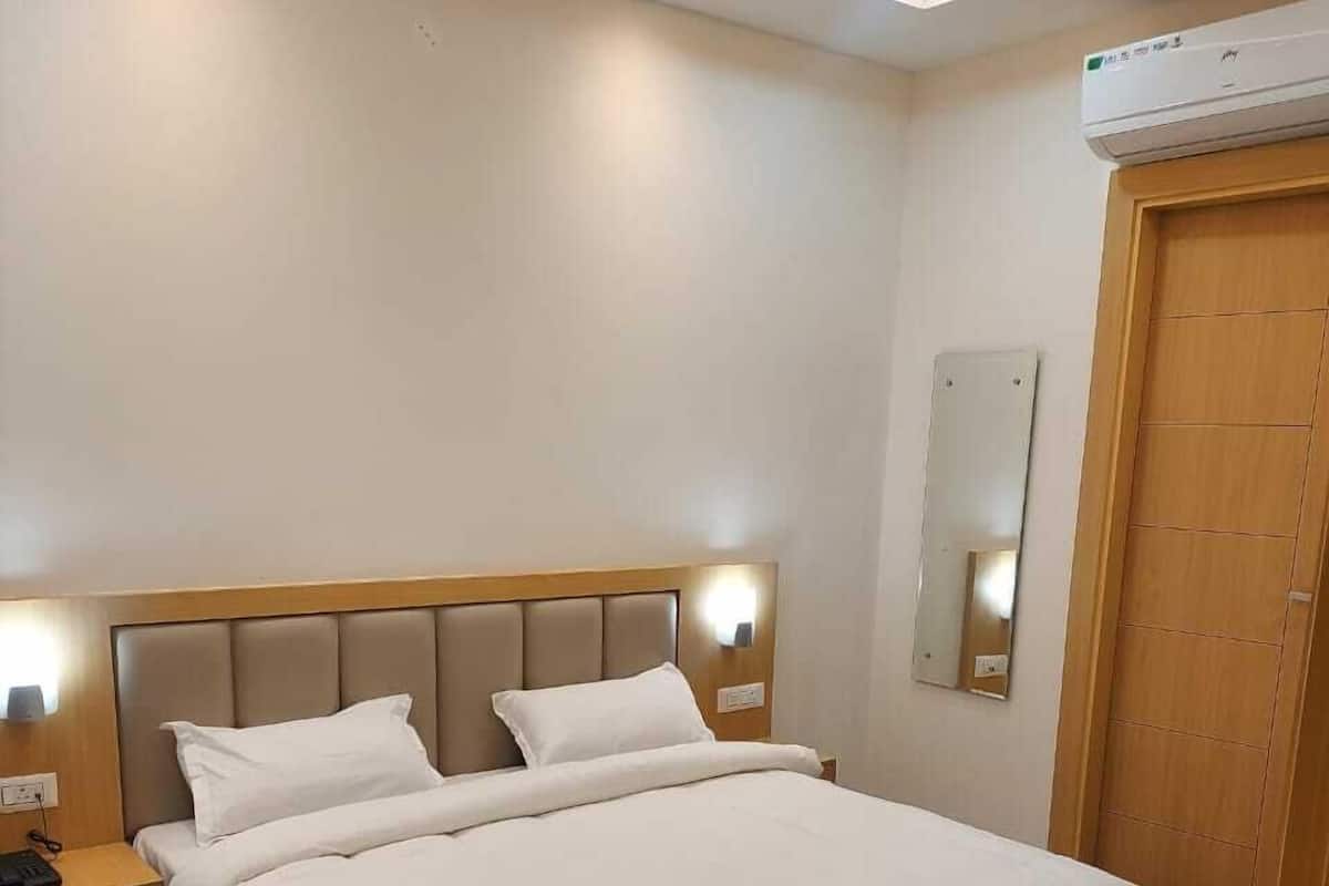 Moderni hotellihuone, jossa on suuri sänky, yöpöydät, yövalaisin, peili ja ilmastointilaite.