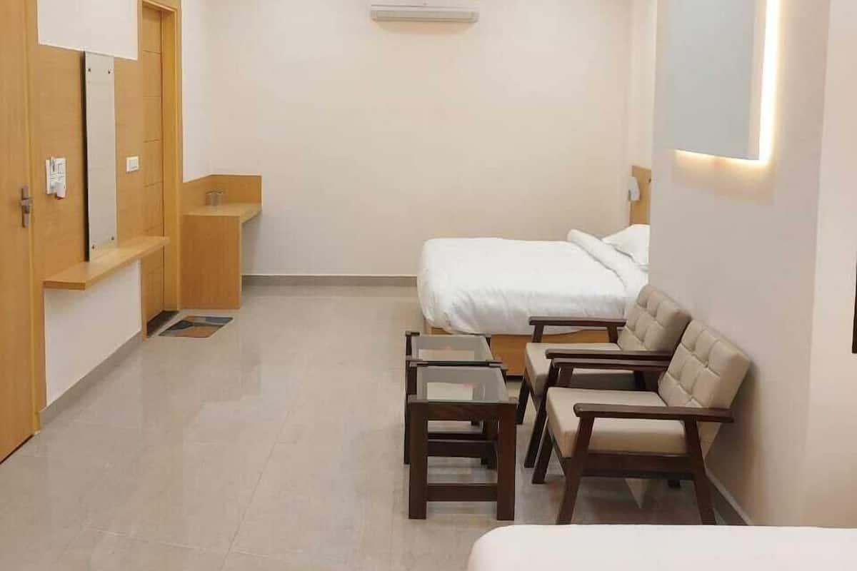 Moderni hotellihuone, jossa on sänky, kaksi nojatuolia, pieni pöytä, kattotuuletin ja ilmastointilaite.