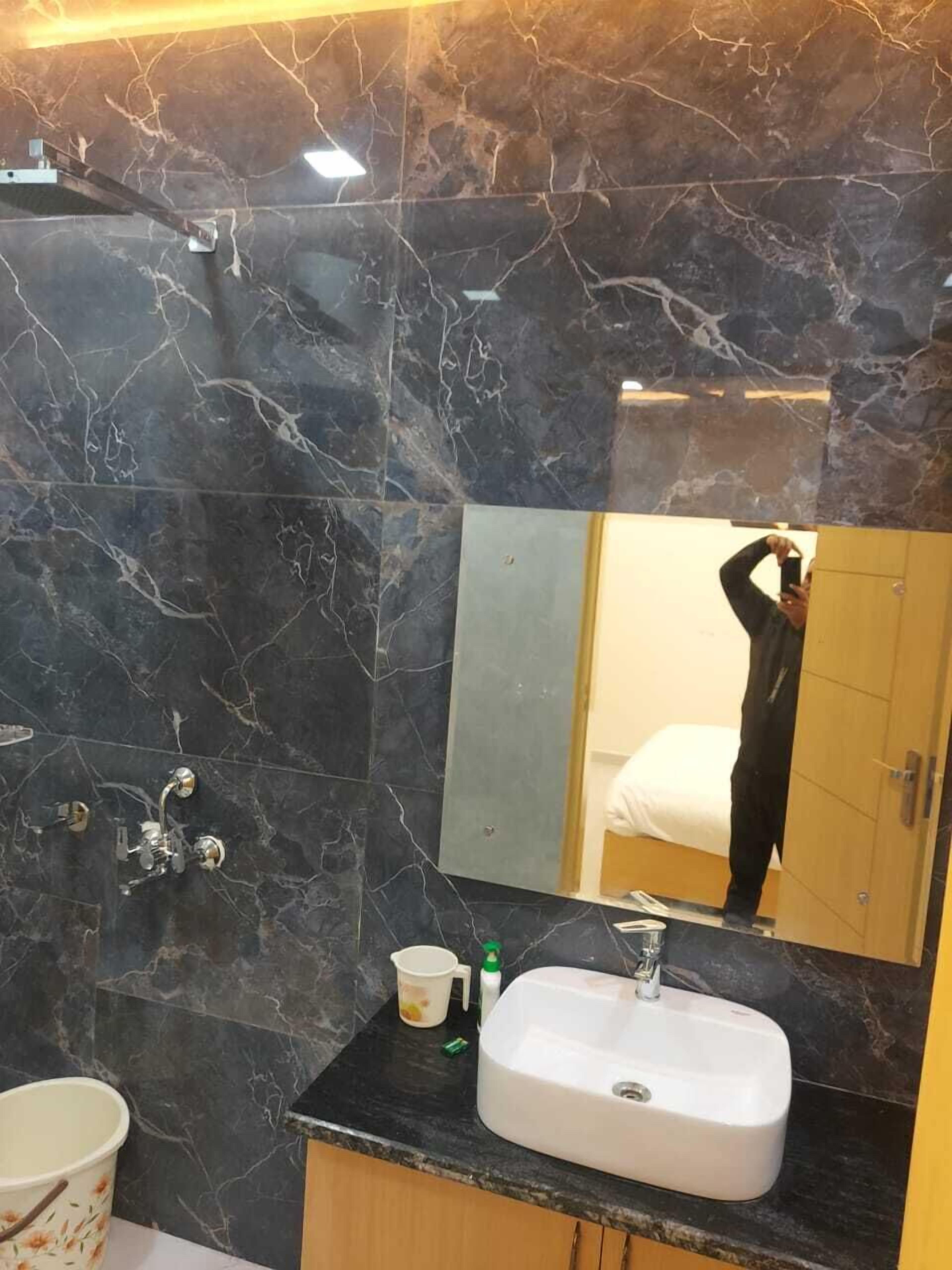 Een badkamer met donkere marmeren wanden, een wit wastafelmeubel, een spiegel en een douchehoek.