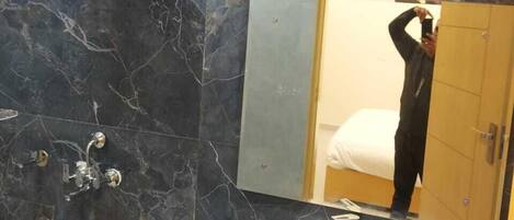 Een badkamer met donkere marmeren wanden, een wit wastafelmeubel, een spiegel en een douchehoek.