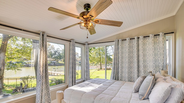 A bedroom with a large bed, a ceiling fan, and multiple windows offering a view of a lake and park. - Waterfront Retreat w/ Hot Tub in Gun Barrel City! (Gun Barrel City)