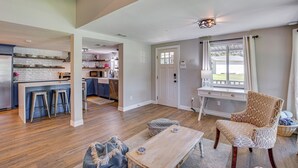 A spacious living area with a wooden floor, a dining table with stools, a patterned armchair, and a kitchen in the background. - Waterfront Retreat w/ Hot Tub in Gun Barrel City! (Gun Barrel City)
