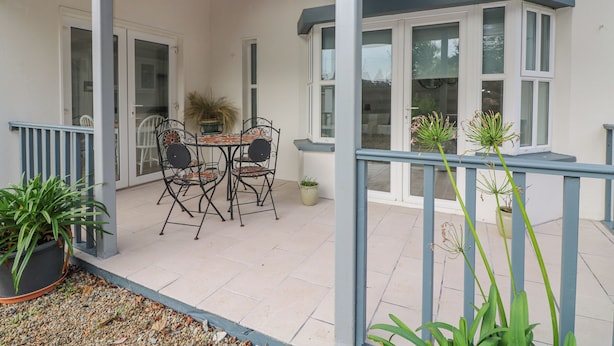 Un patio couvert avec une table et des chaises, une plante en pot et une vue sur la maison à travers une grande baie vitrée.