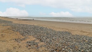 Une plage de galets et de sable, une personne qui se promène et l’océan en arrière-plan.