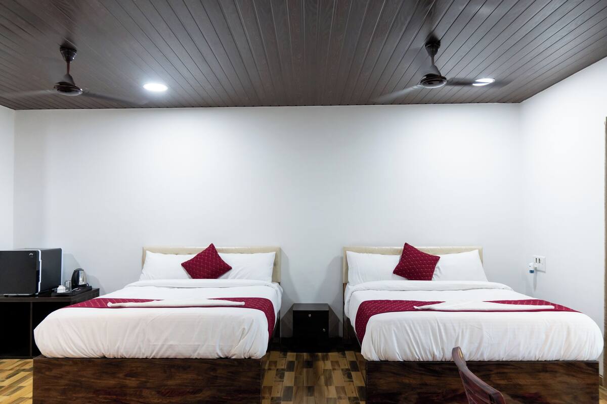 A hotel room with two beds, a desk with a computer, and a ceiling fan.