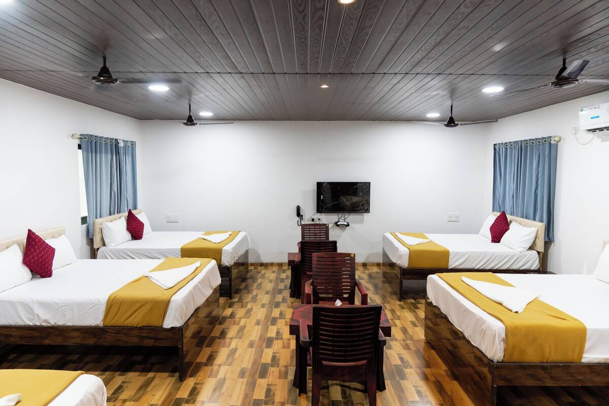 A hotel room with four beds, a wooden floor, ceiling fans, and a flat-screen TV.