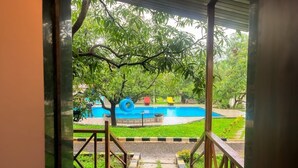 Blick auf einen Pool mit Rutsche, umgeben von üppiger Vegetation und einem überdachten Bereich mit Stufen zum Pool.