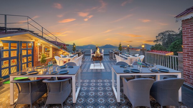Un espace extérieur aménagé pour les repas, avec des tables et des chaises, un foyer et une vue sur les montagnes au coucher du soleil.