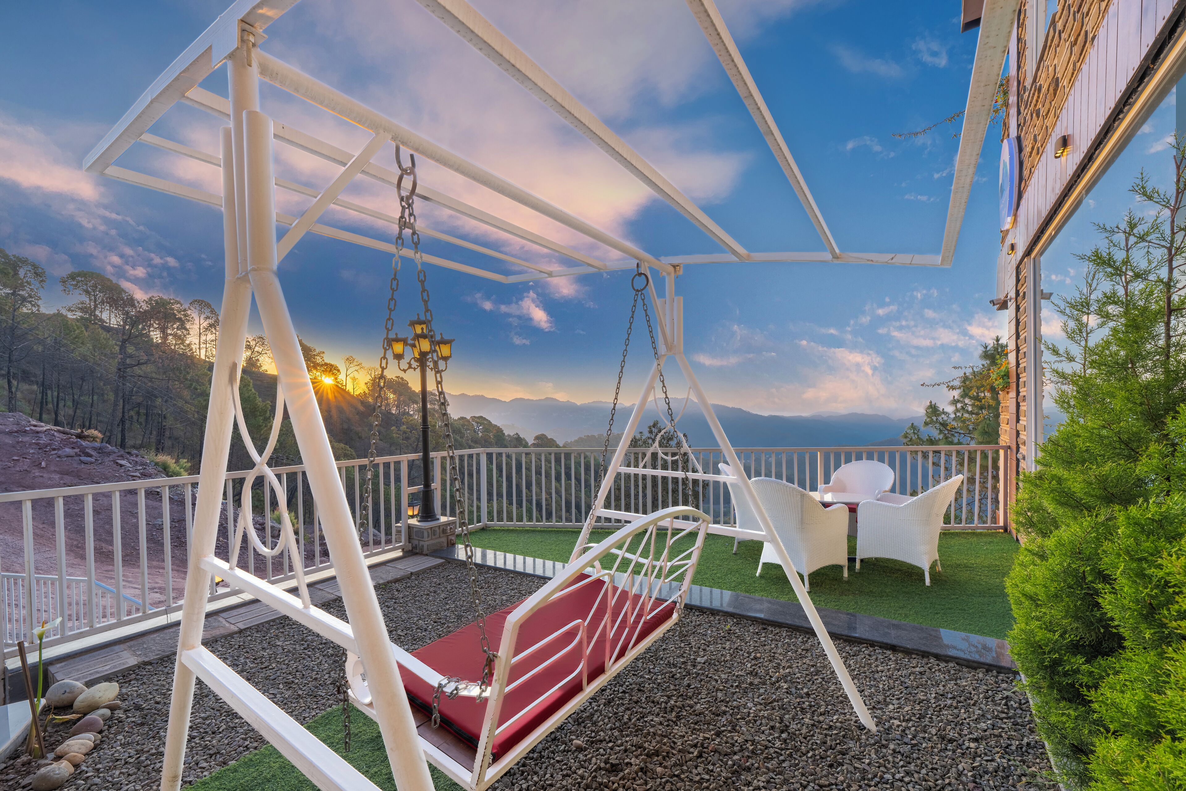 A swing set with a red cushion, white wicker chairs, and a view of the landscape.