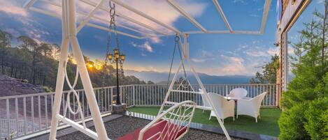 A swing set with a red cushion, white wicker chairs, and a view of the landscape.