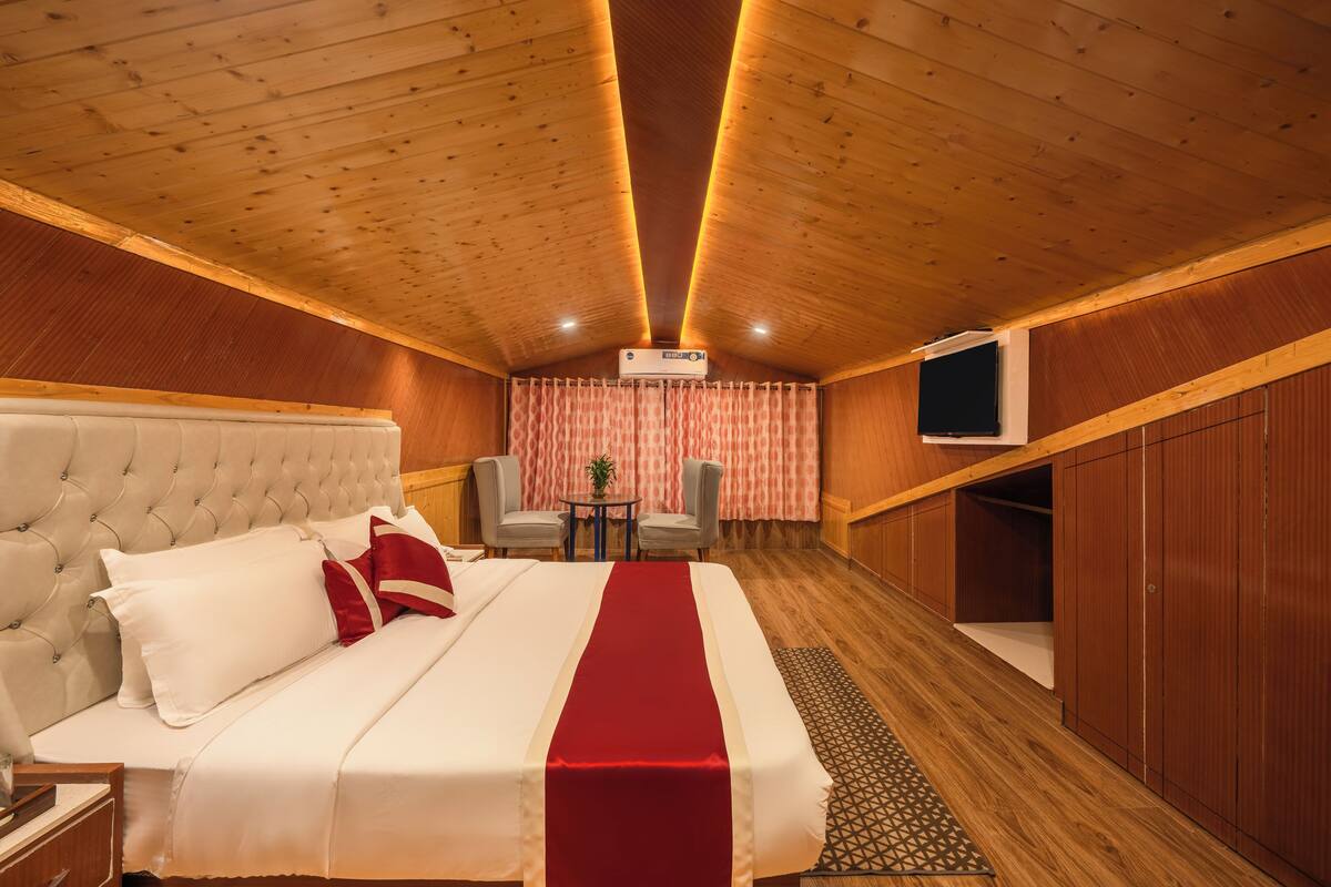 Ein Hotelzimmer mit einem großen Bett, einem Fernseher, einem kleinen Tisch mit Stühlen und einem Fenster mit Vorhängen.