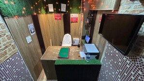 A reception desk with a green artificial turf, a white chair, a computer, and a flat-screen TV. - The Capstone (New Delhi)