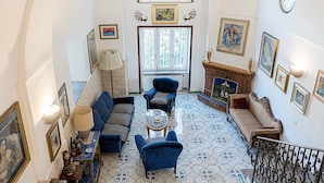 A spacious living room with a high ceiling, a fireplace, and a view of the outside through a large window.