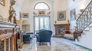 A spacious living room with a high ceiling, a fireplace, and a staircase.