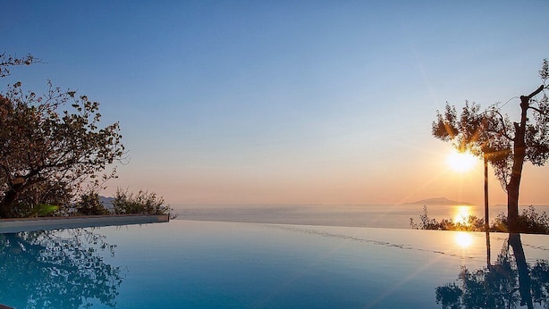 An infinity pool with a clear view of the sunset over the ocean.