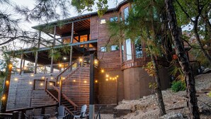 A rustic cabin with a wooden exterior, a staircase leading to a deck, and outdoor seating with Adirondack chairs.