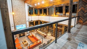 A spacious loft-style room with a stone wall, wooden ceiling, and a large window overlooking a balcony.