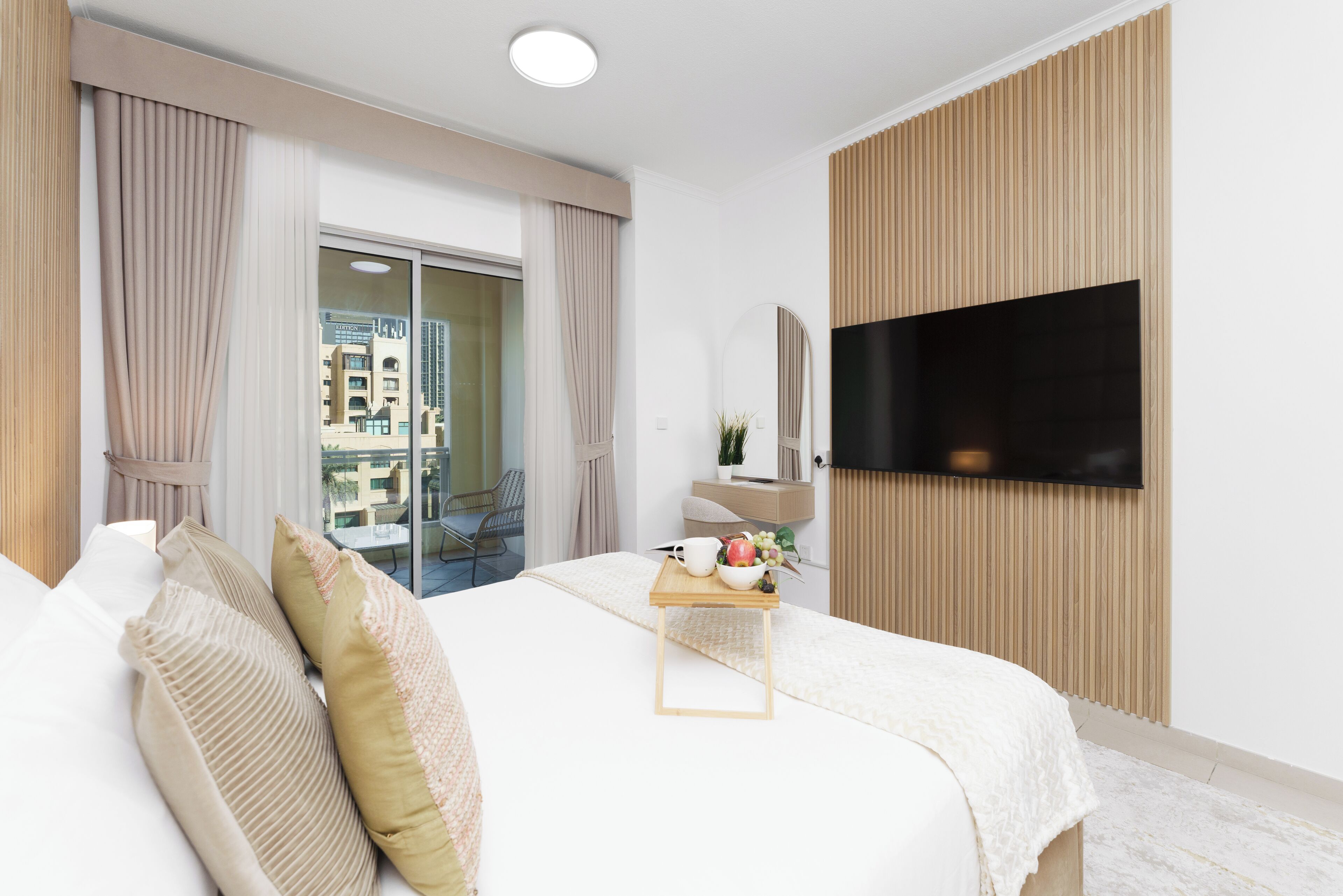A modern hotel room with a large bed, a TV mounted on the wall, and a balcony with a view of the city.