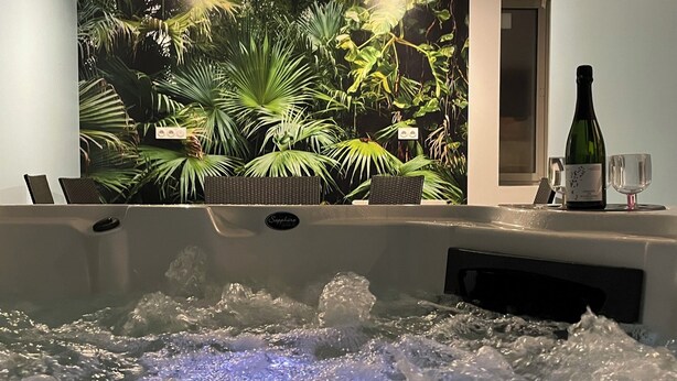 Zona de spa con hidromasaje, una botella de vino y una copa a un lado.