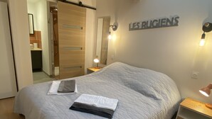 Un dormitorio con una cama grande, techo de madera, una lámpara fijada a la pared y una puerta que da al baño.