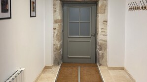 Un pasillo con pared de piedra, una puerta gris y un radiador a la izquierda.