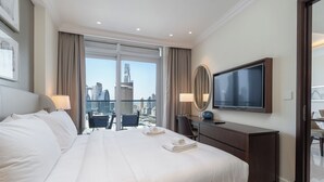 A hotel room with a large bed, a desk, a chair, a TV, and a view of a cityscape through large windows. - Luxury Living Spectacular Burj Views (Dubai)