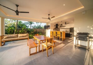 Enjoy a bright and airy living space with a large window offering a view of lush greenery, a dining area, and a modern kitchen with a grill.
