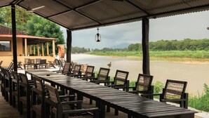 Un espacio de comedor al aire libre cubierto con mesas y sillas largas, con vista a un río.