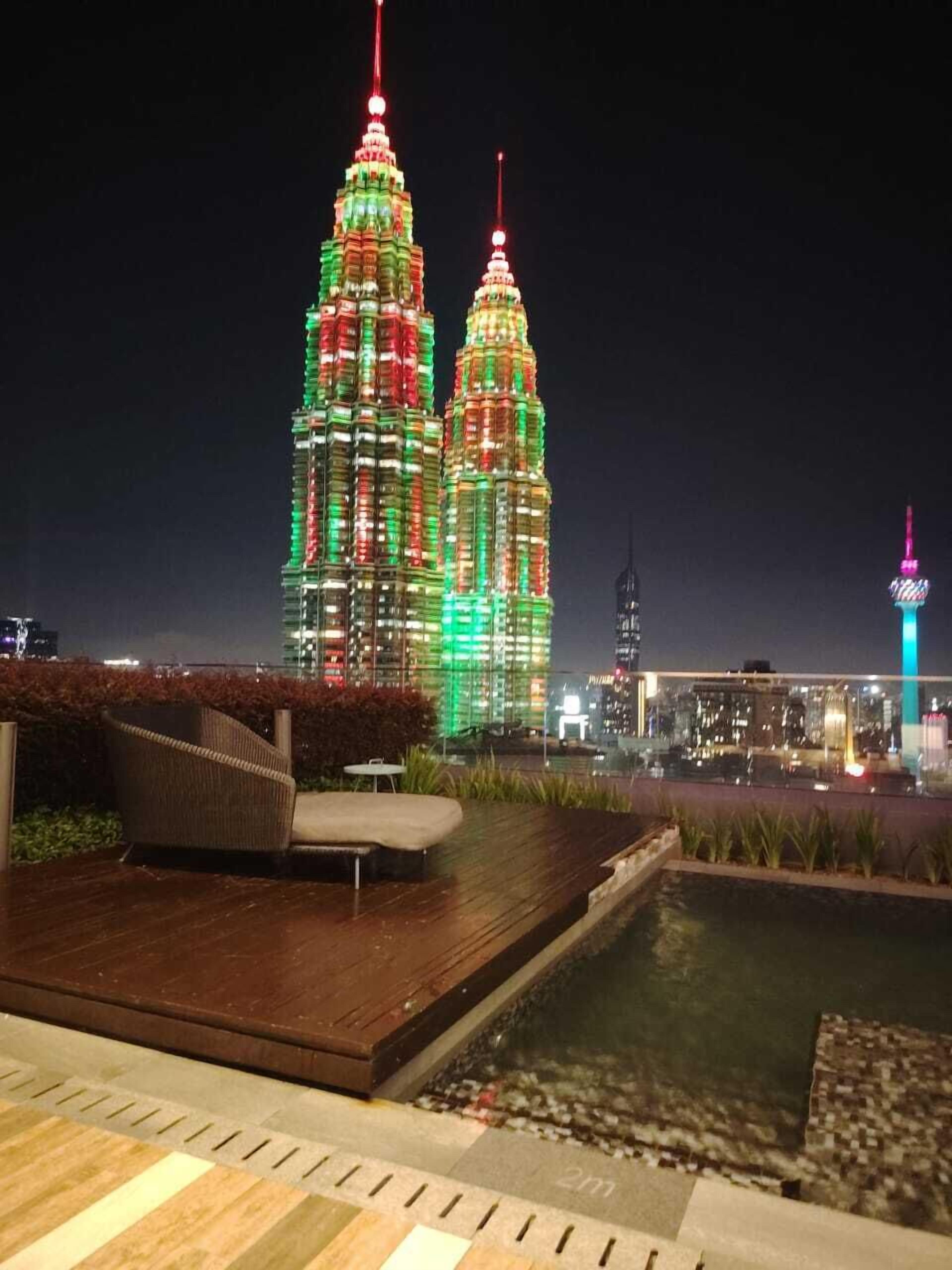 Vue nocturne d’un hôtel avec une piscine, offrant une vue sur les tours Petronas illuminées.
