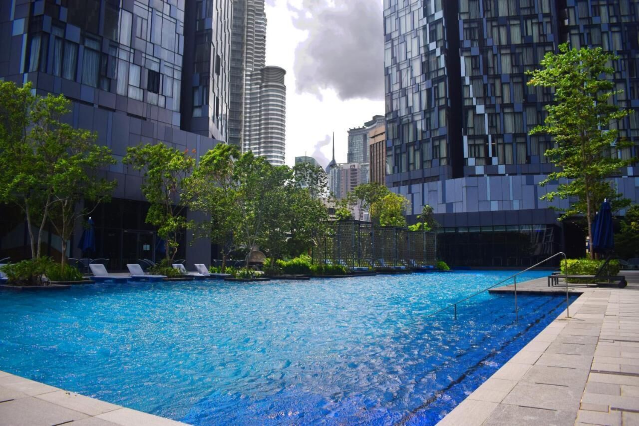 A swimming pool surrounded by modern buildings, trees, and lounge chairs.