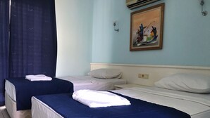 A hotel room with two single beds, a small table, a wall-mounted air conditioner, and a painting above the bed.