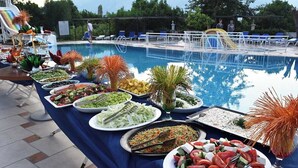 A buffet table with various dishes and a pool in the background.