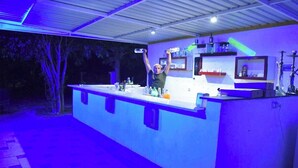 An outdoor bar area with a counter, bar stools, and a variety of bottles and glasses.