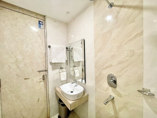 A modern bathroom with a glass shower door, a sink with a mirror, and a towel rack. - Hotel KP - near Sea Beach Puri (Puri)