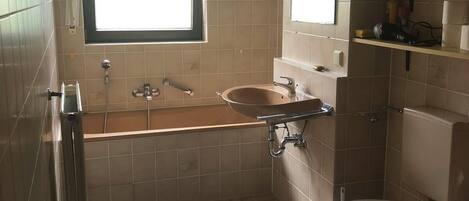A small bathroom with a window, a sink, a toilet, and a shower.