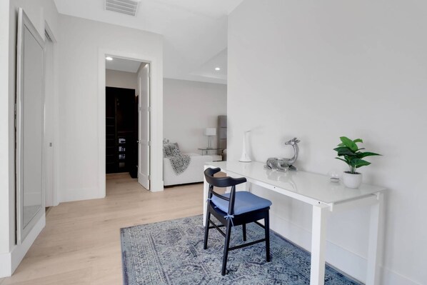 A modern, minimalist room with a white desk, a blue chair, a potted plant, and a patterned rug.